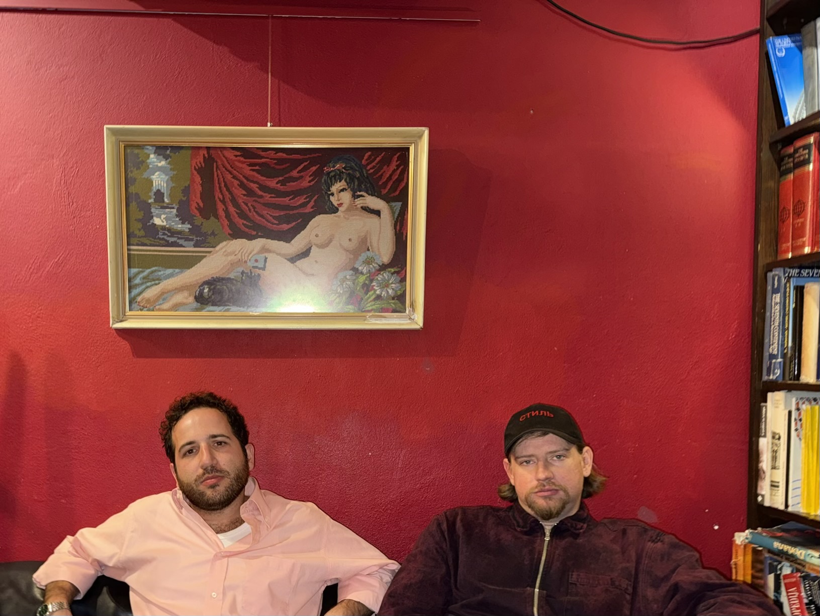 Andrei and Youssef seated together against a red wall